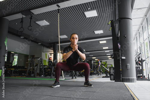 Side view portrait of a young woman doing squats at fitness gym