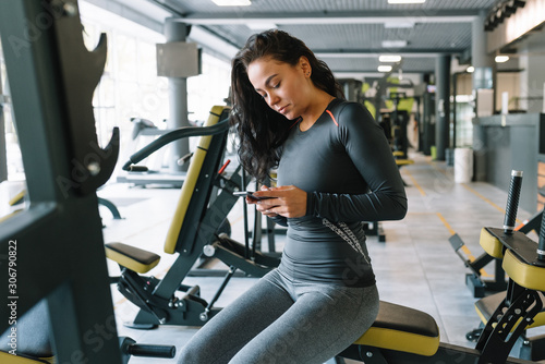 Gorgeous young woman texting and social networking while in a gym