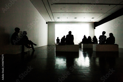 back view of a group of people watching a projected screening in an art gallery 