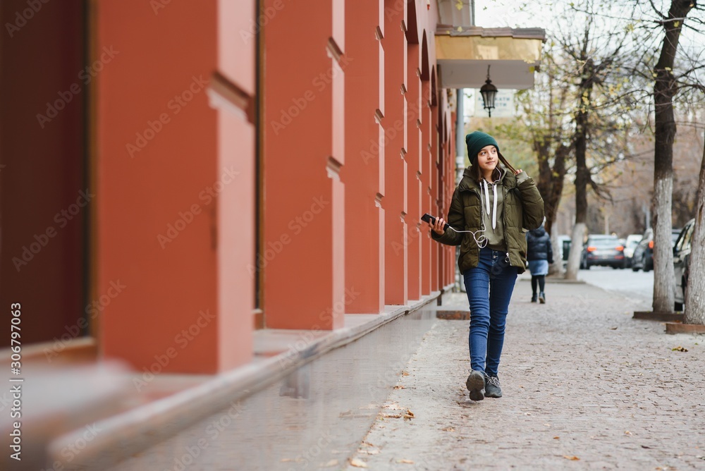 young stylish beautiful teen girl listening to music, mobile phone, headphones, enjoying, denim outfit, smiling, happy, cool accessories, having fun, laughing, park