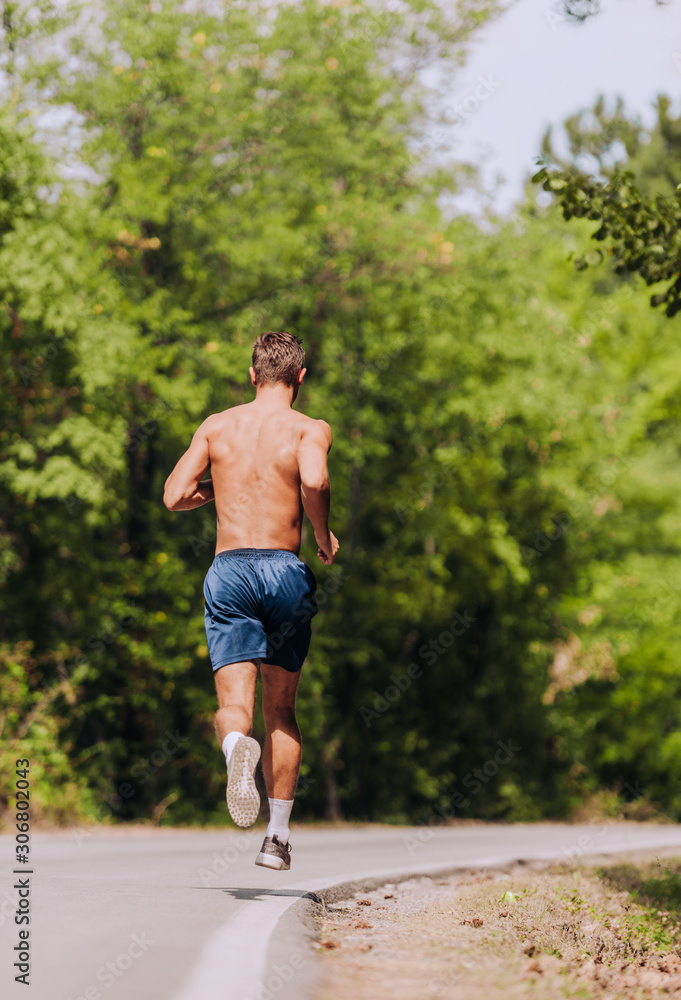 Muscular fit sport model sprinter exercising sprint on forest road Muscular fit sport model sprinter exercising sprint on forest road