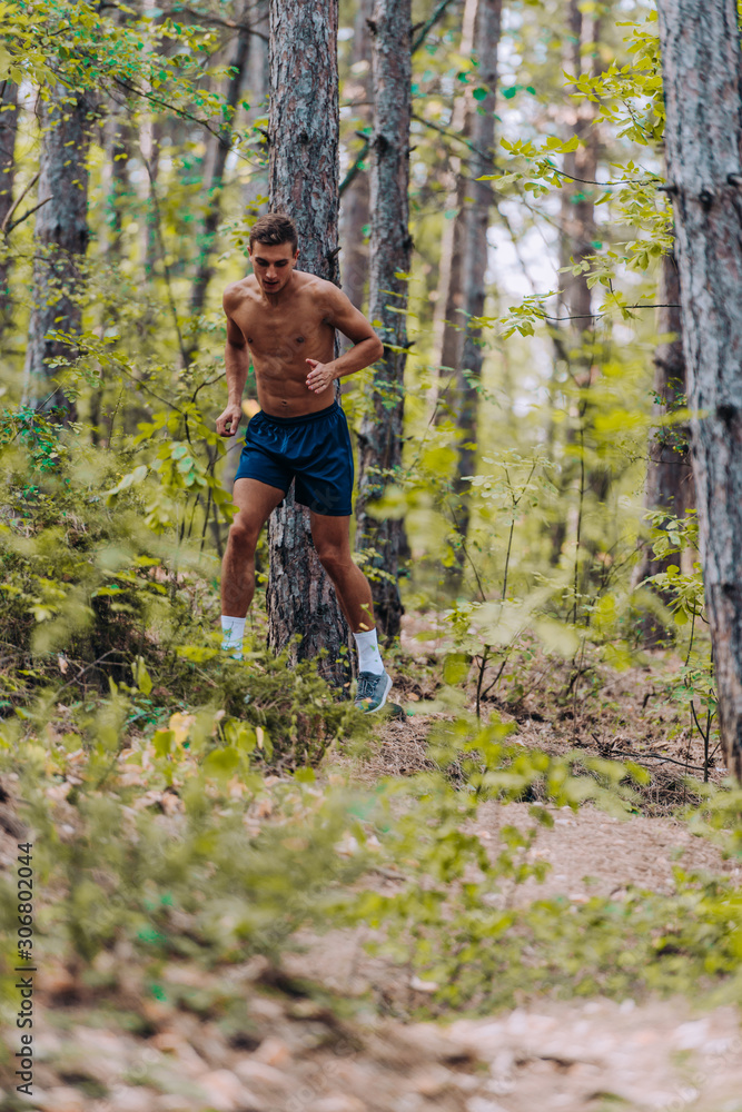 Male shirtless joger running in mountains under trees Male shirtless joger running in mountains under trees