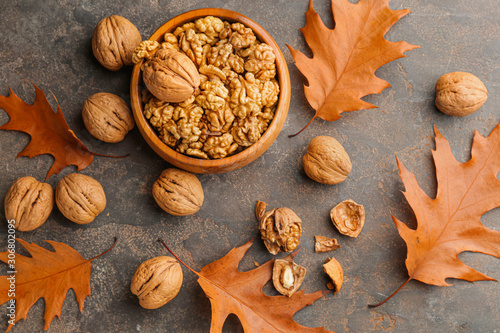 Bowl with tasty walnuts and autumn leaves on grey background