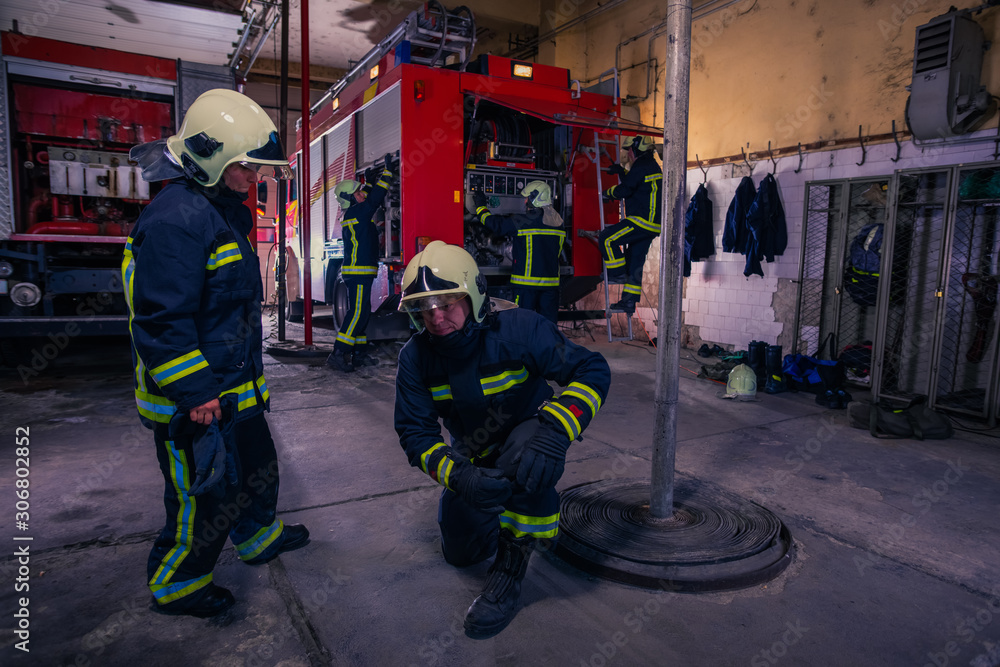 Firefighters preparing their uniform and the firetruck in the background inside the fire station