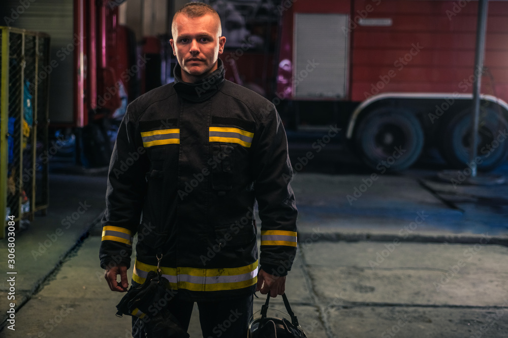 Fototapeta premium Portrait of young fireman standing inside the fire station.