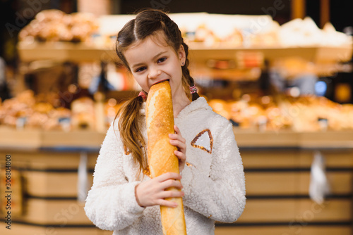 Young and funny girl eating baguettes in front of the bakery store