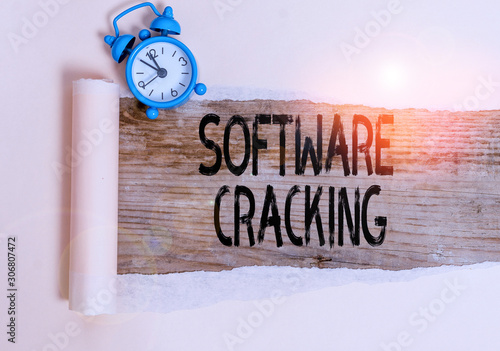 Text sign showing Software Cracking. Business photo showcasing modification of software to remove or disable features Alarm clock and torn cardboard placed above a wooden classic table backdrop photo