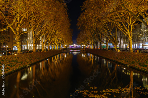 Night view of canal at Königsallee, famous shopping street, and background of Triton Fountain and Ice skate pavilion of Christmas Market from Girardet-Brücke in winter season.