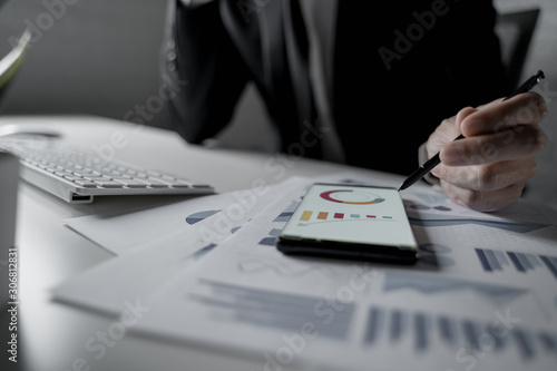 Close up shot of businessman working in office holding smart phone and checking diagrams