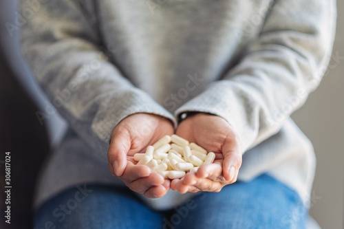 Closeup image of a woman holding white medicine capsules in hand