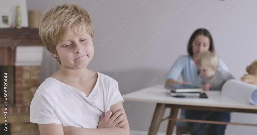 Close-up of sad Caucasian boy with grey eyes looking back at his sister and mother, turning back and looking away. Guy in white T-shirt posing at home. Cinema 4k ProRes HQ. Close-up of sad Caucasian boy with grey eyes looking back at his sister and mother, turning back and looking away. Guy in white T-shirt posing at home. Cinema 4k ProRes HQ.