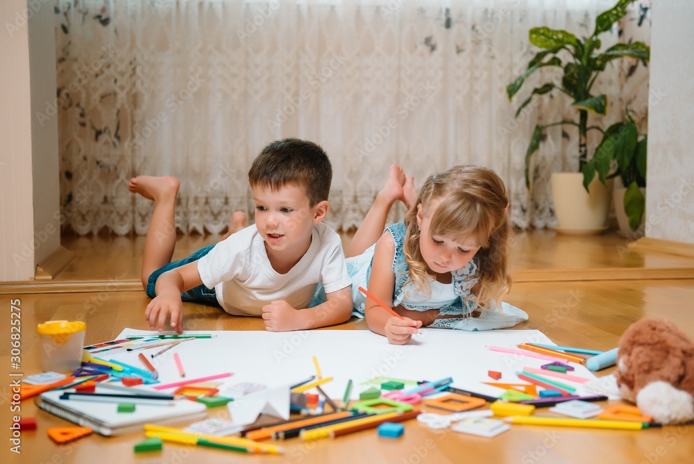 Kids drawing on floor on paper. Preschool boy and girl play on floor with educational toys - blocks, train, railroad, plane. Toys for preschool and kindergarten. Children at home or daycare. Kids drawing on floor on paper. Preschool boy and girl play on floor with educational toys - blocks, train, railroad, plane. Toys for preschool and kindergarten. Children at home or daycare.