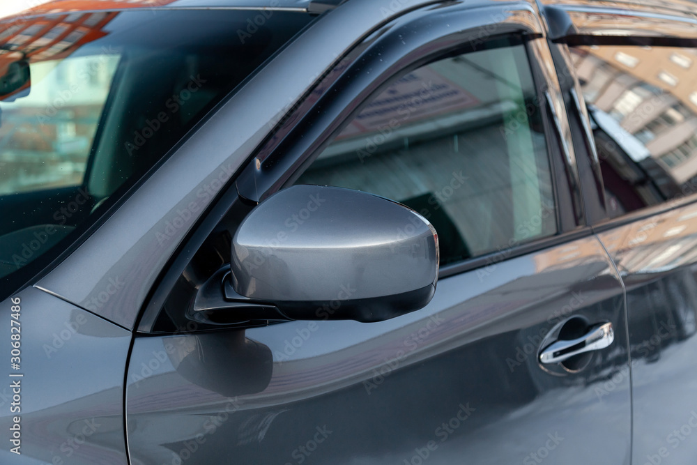 Close-up of the side left mirror without turn signal repeater and window of the car body gray SUV on the street parking after washing and detailing in auto service industry. Road safety while driving Close-up of the side left mirror without turn signal repeater and window of the car body gray SUV on the street parking after washing and detailing in auto service industry. Road safety while driving