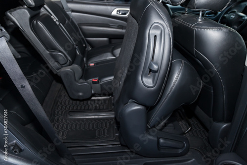 Clean after washing the rear passenger seats of matte black genuine leather inside the interior with three rows and seven seater of an expensive SUV, preparation before selling the car. © Aleksandr Kondratov