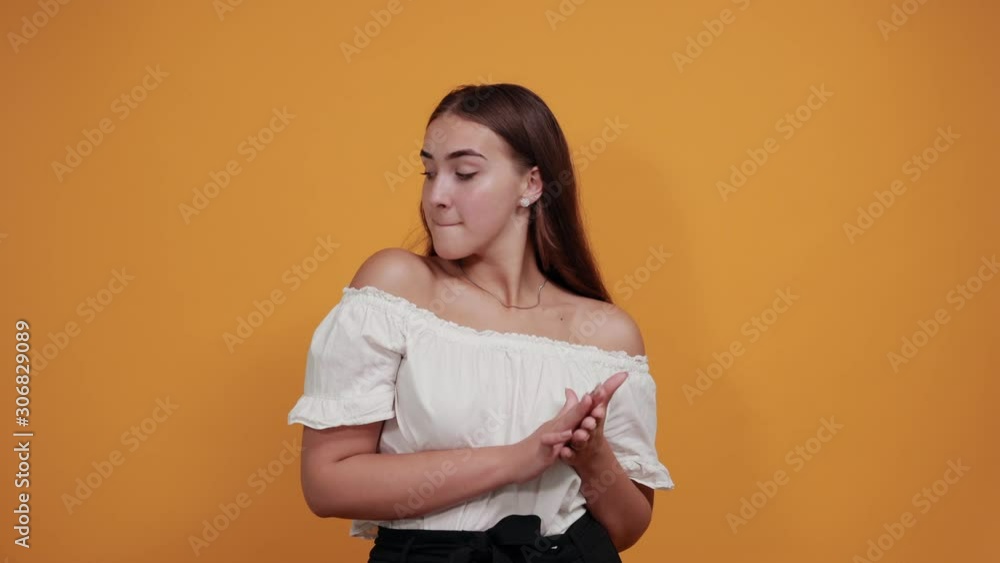 Cheerful young woman keeping hands together, looking at camera, funny, smiling girl isolated on orange background in studio in casual white shirt. People sincere emotions, lifestyle concept. Cheerful young woman keeping hands together, looking at camera, funny, smiling girl isolated on orange background in studio in casual white shirt. People sincere emotions, lifestyle concept.