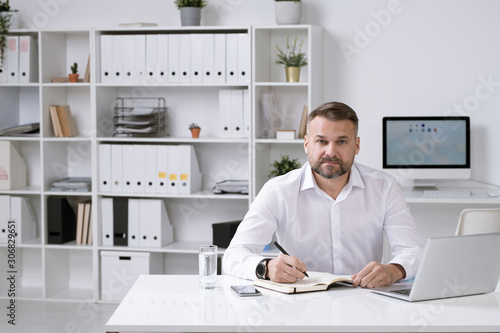 Confident employer in white shirt sitting in his office and organizing work
