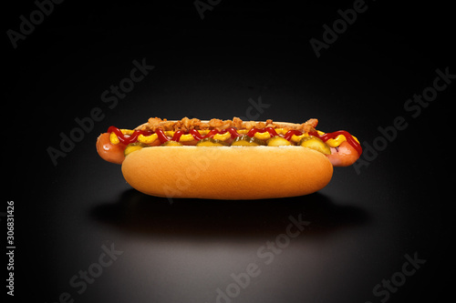 Danish hot dog with pickled cucumbers, fried onions, ketchup and mustard on a black background.