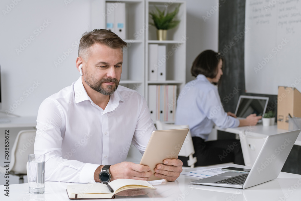 Serious office worker looking at touchpad display while watching online training Serious office worker looking at touchpad display while watching online training