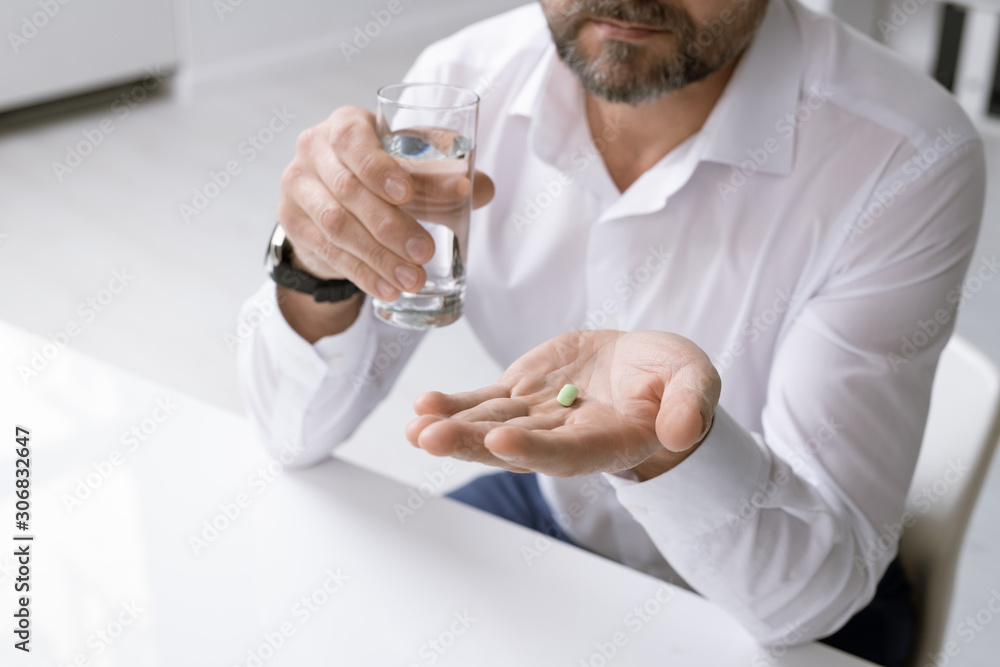 Elegant man in formalwear holding glass of water and painkiller over desk Elegant man in formalwear holding glass of water and painkiller over desk