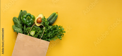 Shopping bag full green vegetables on yellow background with copy space  Purchase healthy food concept
