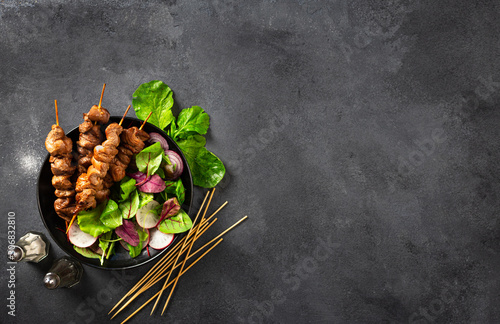 Chicken shish kebab with salad in plate on dark background with place for your text top view