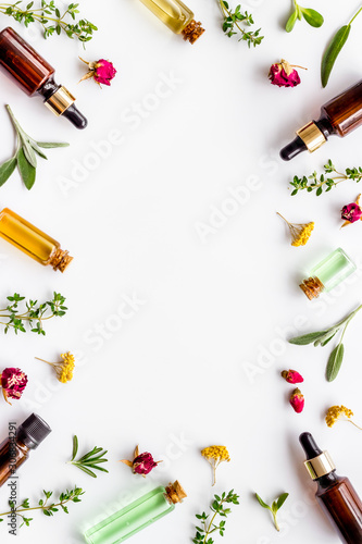 Natural wellness. Essential oils near herbs and leaves on white background top view pattern frame copy space