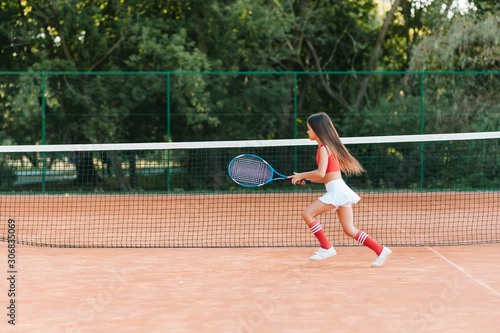 Child playing tennis on outdoor court. Little girl with tennis racket and ball in sport club. Active exercise for kids. Summer activities for children. Training for young kid. Child learning to play © Serhii