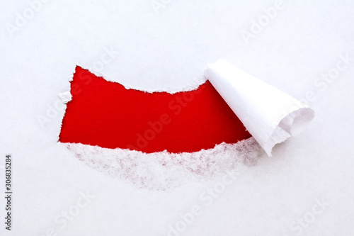 A hole in white paper with torn edges with a bright red color paper background inside. Good paper texture.
