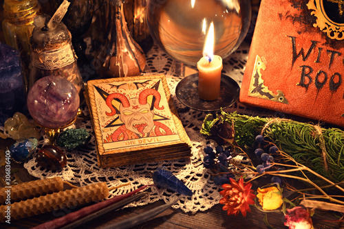 Still life with tarot card Devil, witch book, crystal ball, candle and herbs on wooden table.