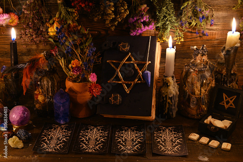 Still life with pentagram book, tarot cards, runes dry flowers and herbs on witch table.