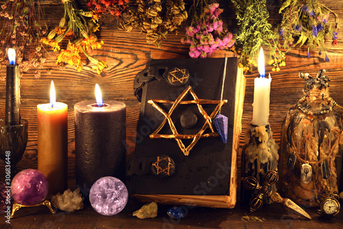 Evil book with pentagram, buning candles, crystal ball, elixir and herbs on witch table. photo