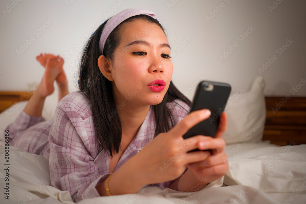 young beautiful and sweet Asian Chinese woman in cute pajamas playful in bed using mobile phone enjoying social media or online dating app happy and relaxed young beautiful and sweet Asian Chinese woman in cute pajamas playful in bed using mobile phone enjoying social media or online dating app happy and relaxed