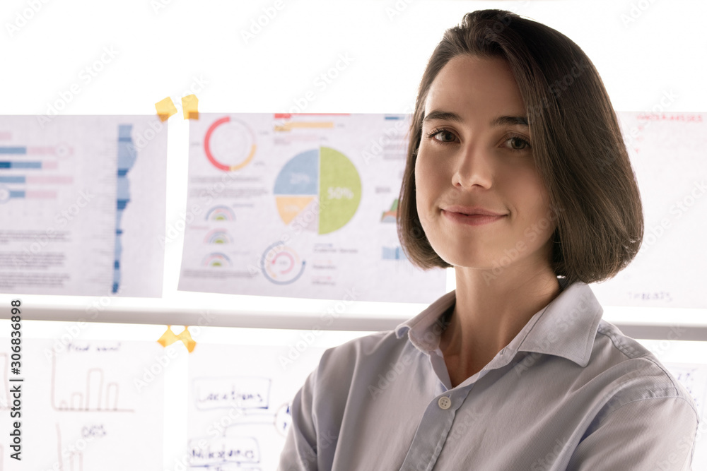 Pretty young smiling broker standing in front of camera against whiteboard Pretty young smiling broker standing in front of camera against whiteboard