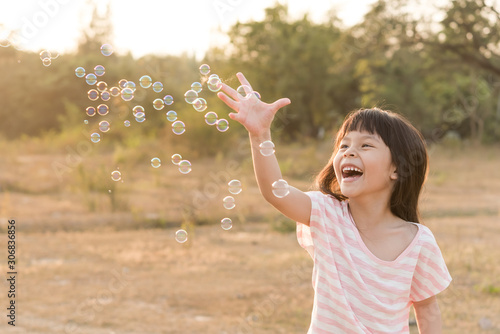 portrait of funny little girl catching soap bubbles in the summer on nature. Background toning instagram filter. little asian girl blowing bubbles in field. happy childhood concept.