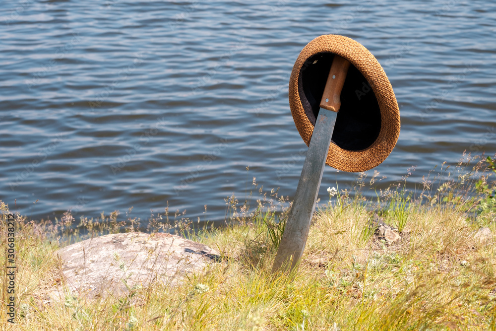 Fototapeta premium hat worn on a sword stuck in the ground on the shore of the pond