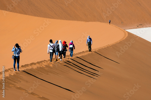 Fototapeta Naklejka Na Ścianę i Meble -  Travelers walking on the sand dune desert with clear blue sky background.