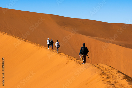 Travelers walking on the sand dune desert with clear blue sky background.