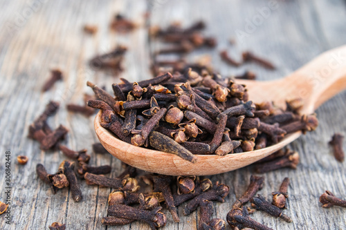 A spice of dried cloves lies on a wooden spoon and is scattered on old wooden boards.