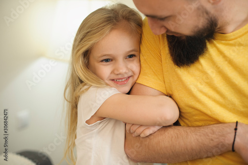Smiling girl embracing her father from arm. Father and daughter spending happy time together at home.