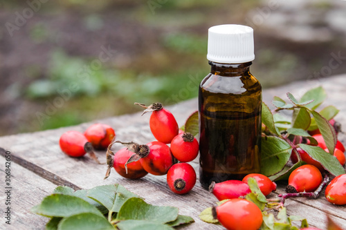Rosehip seed essential oil in a bottle near ripe red rosehip berries. Tincture or essential oil with rose hips.