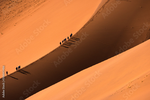Fototapeta Naklejka Na Ścianę i Meble -  Aerial view group of Traveler walking on the sand dune in the desert and sun gradually create beautiful scene.