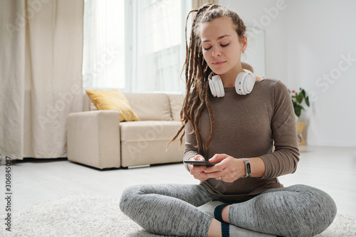Girl with dreadlocks scrolling in smartphone while sitting with crossed legs