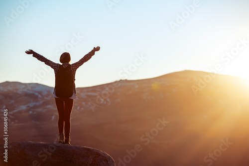 Girl stands with raised arms against sunset light