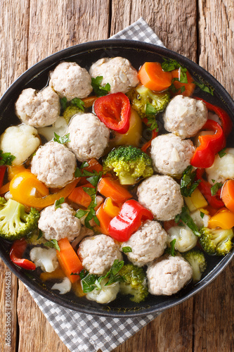 Vegetable soup with chicken meatballs close-up in a plate. Vertical top view
