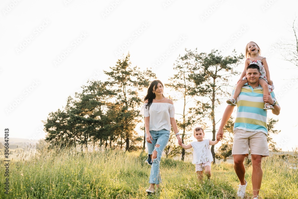 Fototapeta premium Color photo of smiling young parents and two children, rest and have fun in nature. Love, family and happy childhood lifestyle concept