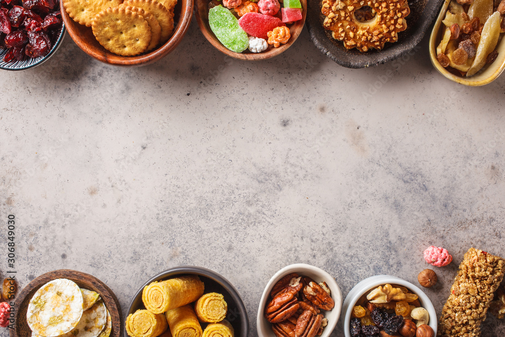 Variety of snacks and sweets on gray background. Waffles, nuts, sweets, cookies, chips and fruits, top view. Variety of snacks and sweets on gray background. Waffles, nuts, sweets, cookies, chips and fruits, top view.