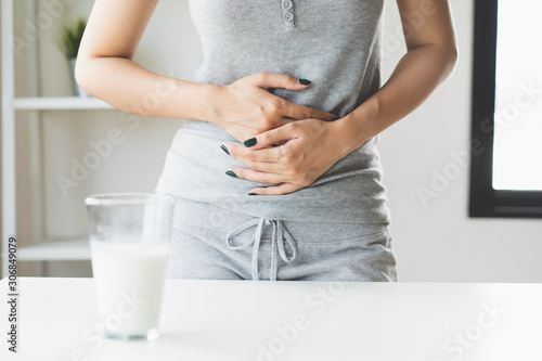 lactose intolerance concept. Woman holding a glass of milk and having a stomachache. photo