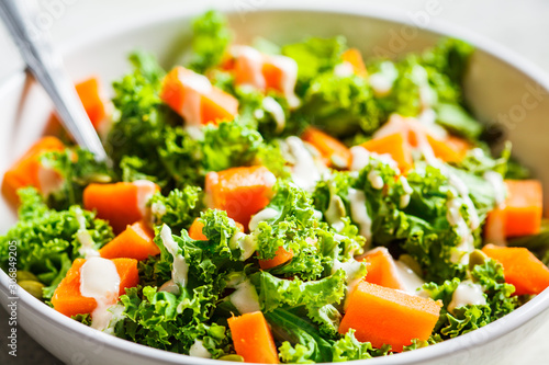 Kale and baked sweet potato salad with tahini dressing in white bowl. Healthy vegan food concept.