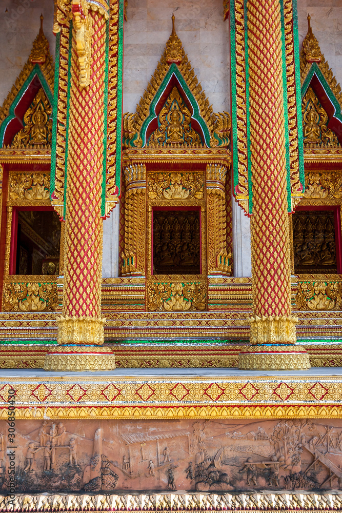 Chic gilded columns and windows of a Buddhist temple with beautiful ornaments. Sacred plots are molded from clay below. Vertical orientation.