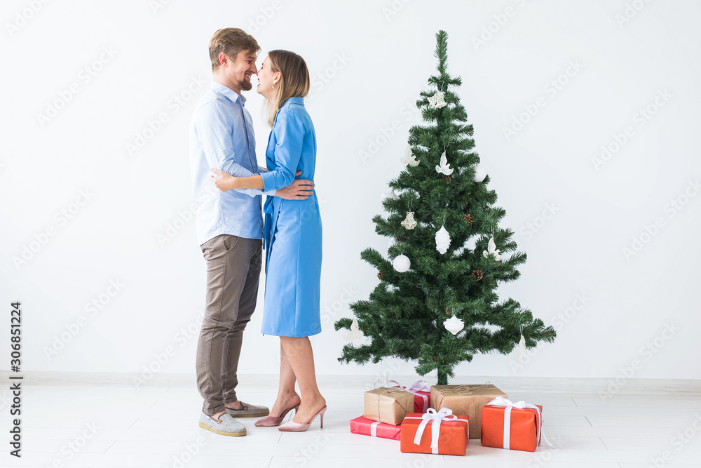 Holidays and festive concept - Young happy couple near a Christmas tree on white background Holidays and festive concept - Young happy couple near a Christmas tree on white background